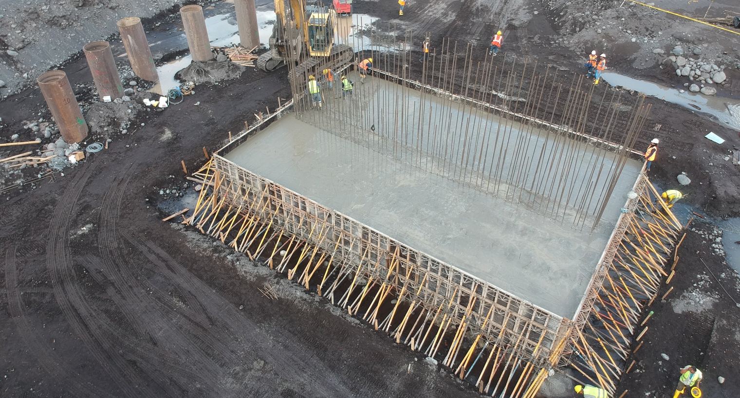 Aerial view of a pile cap being poured, with a row of steel pile casings beside it